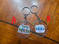 Two keychains with 'Army Mom' text on clear acrylic backgrounds, on a wooden surface.