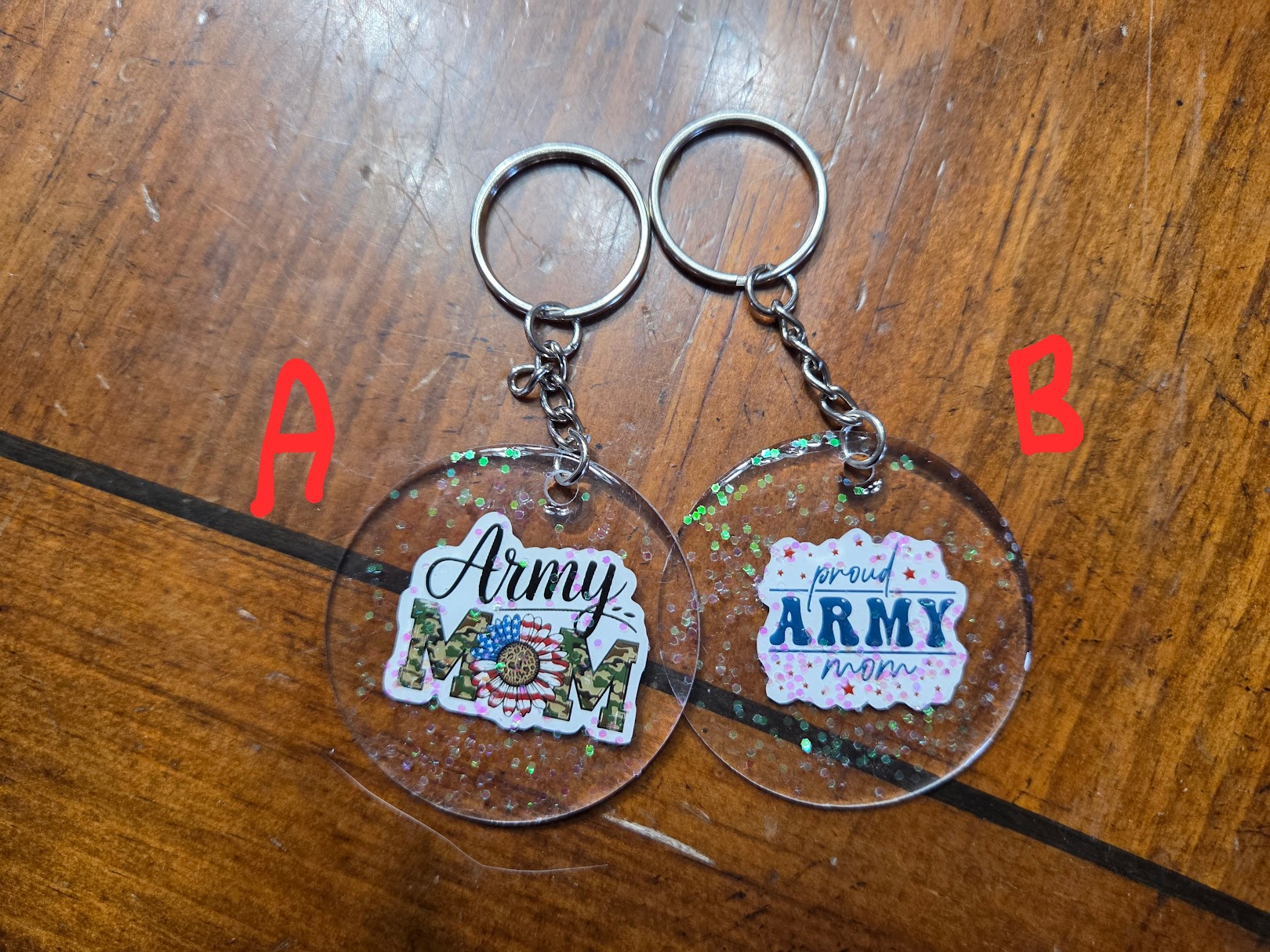 Two keychains with 'Army Mom' text on clear acrylic backgrounds, on a wooden surface.