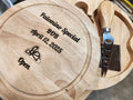 Wooden cutting board with engraved text and a cheese knife on a blurred background