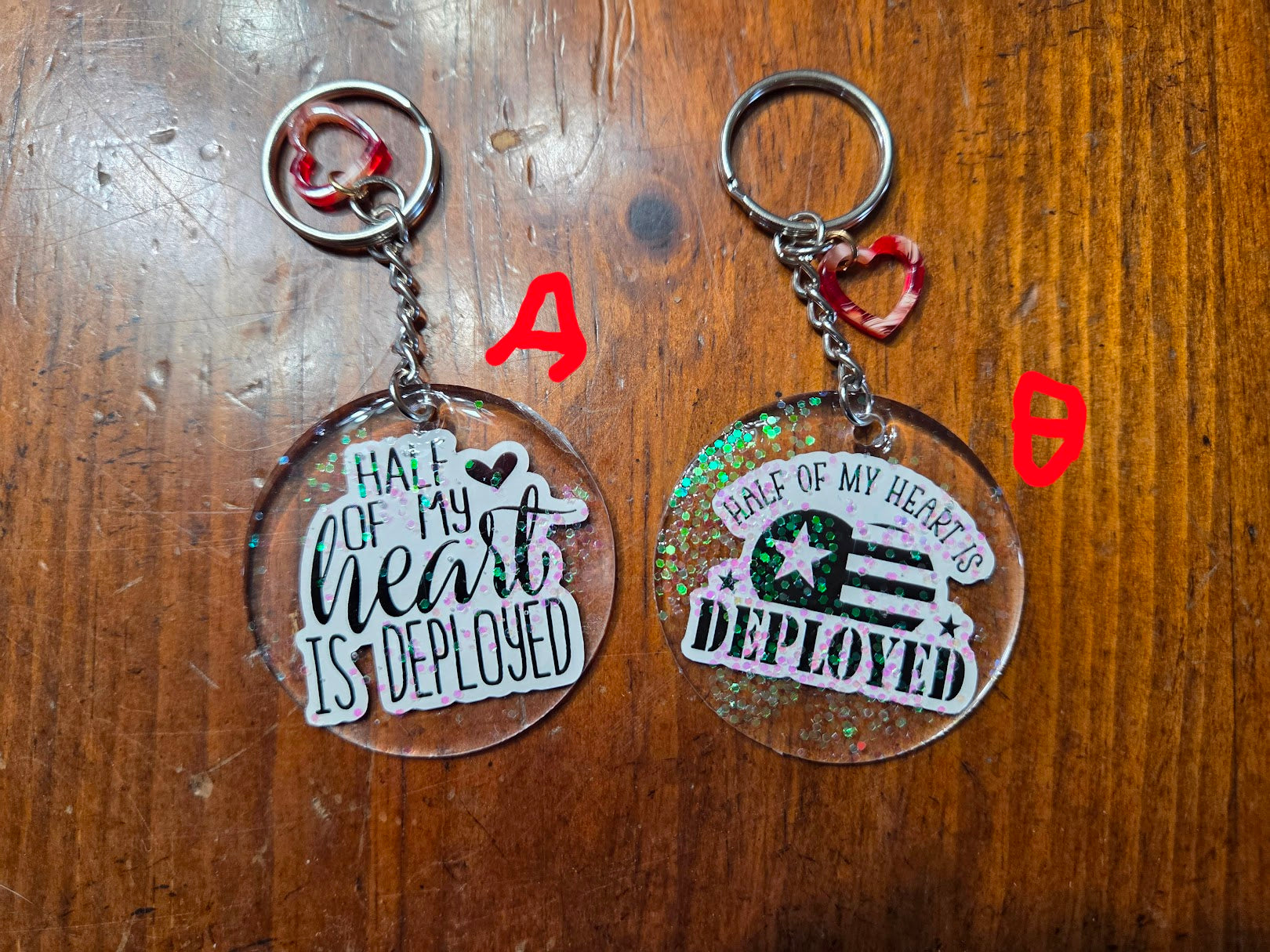 Two keychains with 'Half of my heart is deployed' text on a wooden surface.