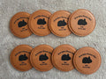 Set of eight brown leather coasters with black bear illustrations and text on a gray surface.