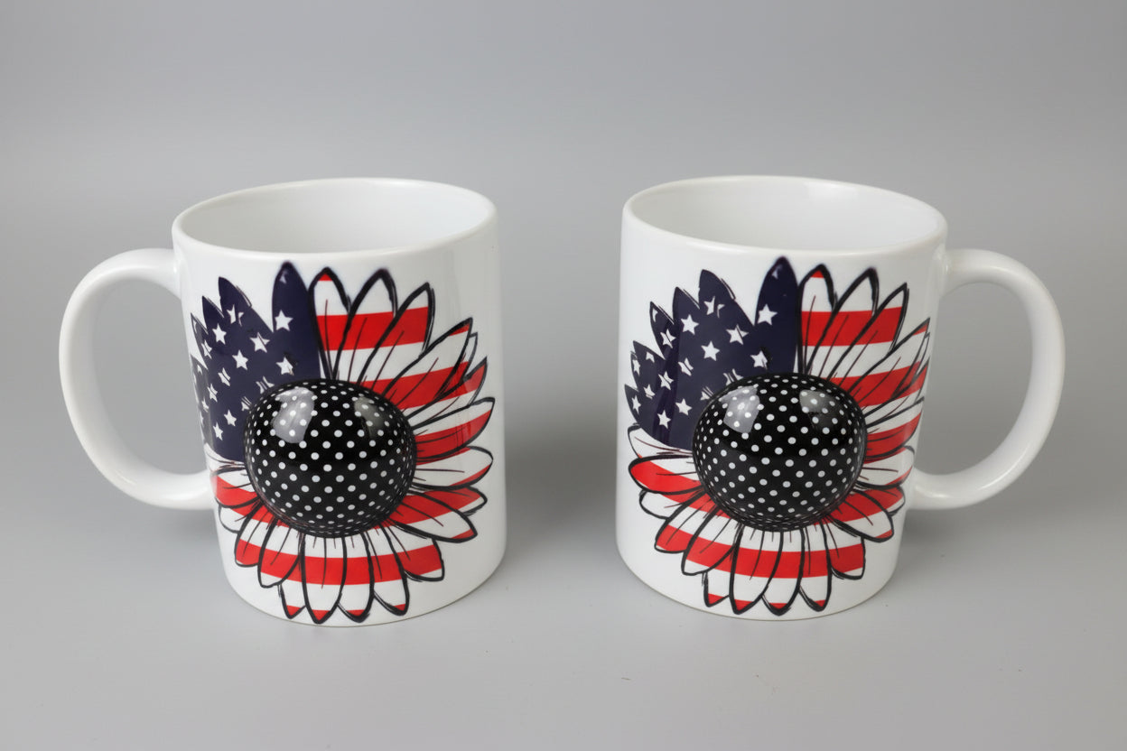 Two mugs with sunflower designs featuring American flag colors on a reflective surface.